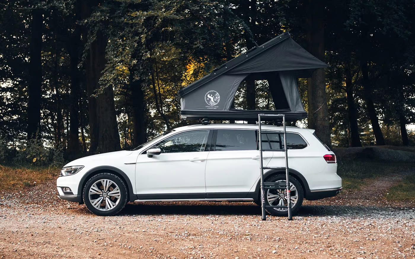 A roof tent set up on top of a car at a UK campsite, showing the ladder and open canopy